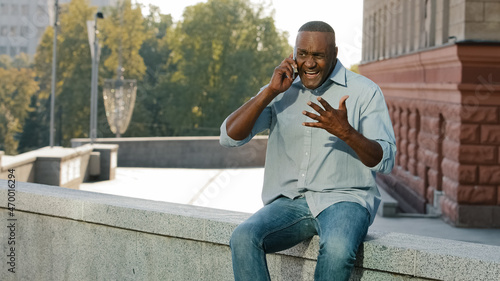 Tablou pe pânză Worried nervous African American man in shirt and jeans holding mobile phone