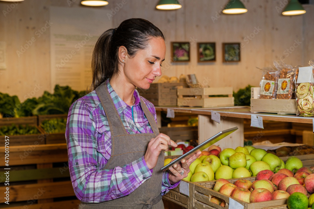 Portrait of a busy female sales assistant in a grocery typing on the tablet while taking inventory - Owner with digital tablet preparing online grocery order
