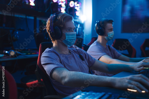 Two guys in medical masks in a computer club feeling involved and concentrated