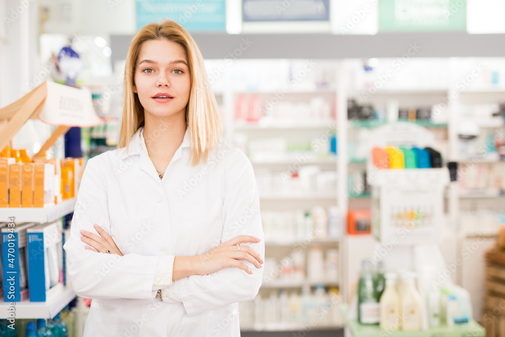 Cheerful woman pharmacist standing with arms crossed in interior of pharmacy. High quality photo
