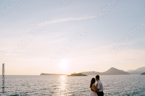 Bride and groom are embracing and looking at the sea