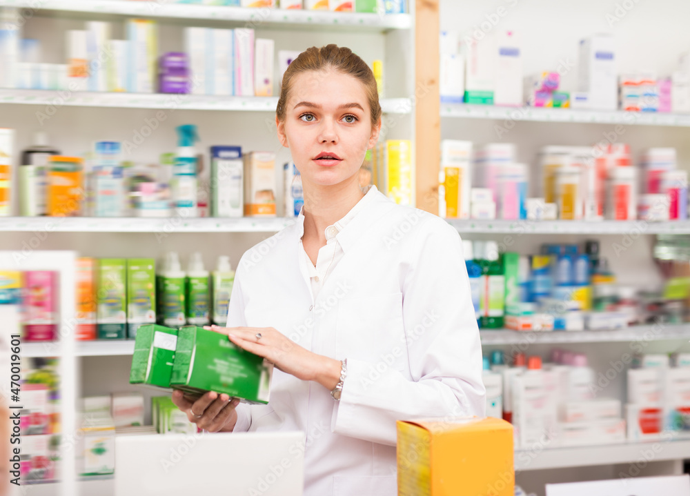 Positive female druggist in white coat working in pharmacy