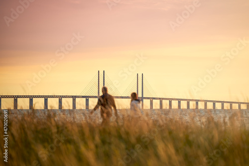 A couple looks out over the Öresund strait with the Öresund Bridge between Sweden and Denmark during sunset in Limhamn, Malmö. photo