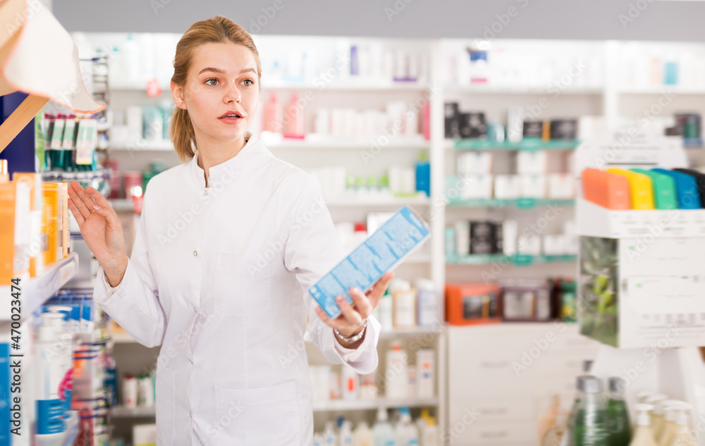 Ordinary female pharmacist offering help in choosing at counter in pharmacy