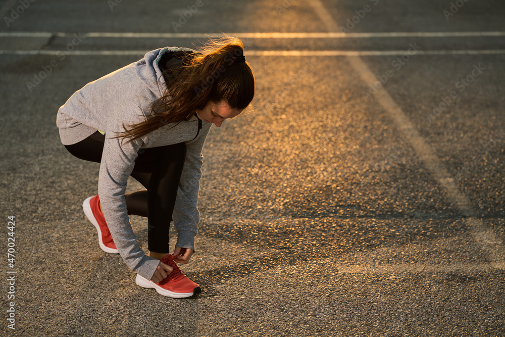 long-haired sportswoman tying her laces on the asphalt ready to practice sport