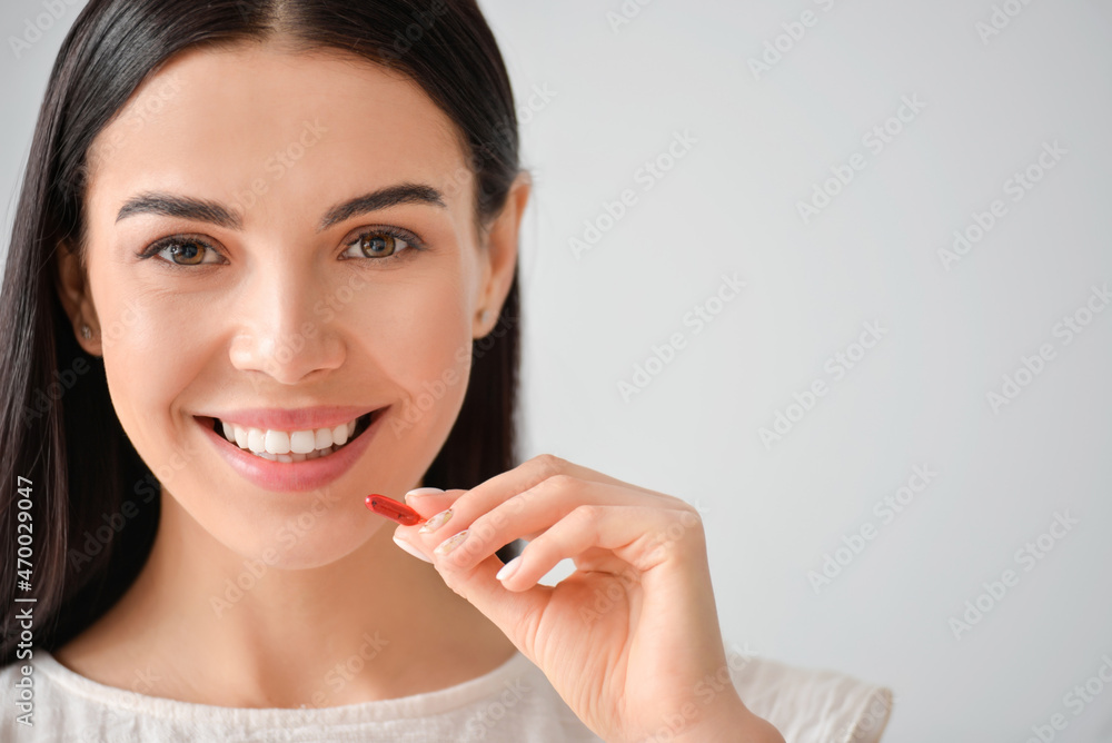 Young woman with pill on grey background Young woman with pill on grey background