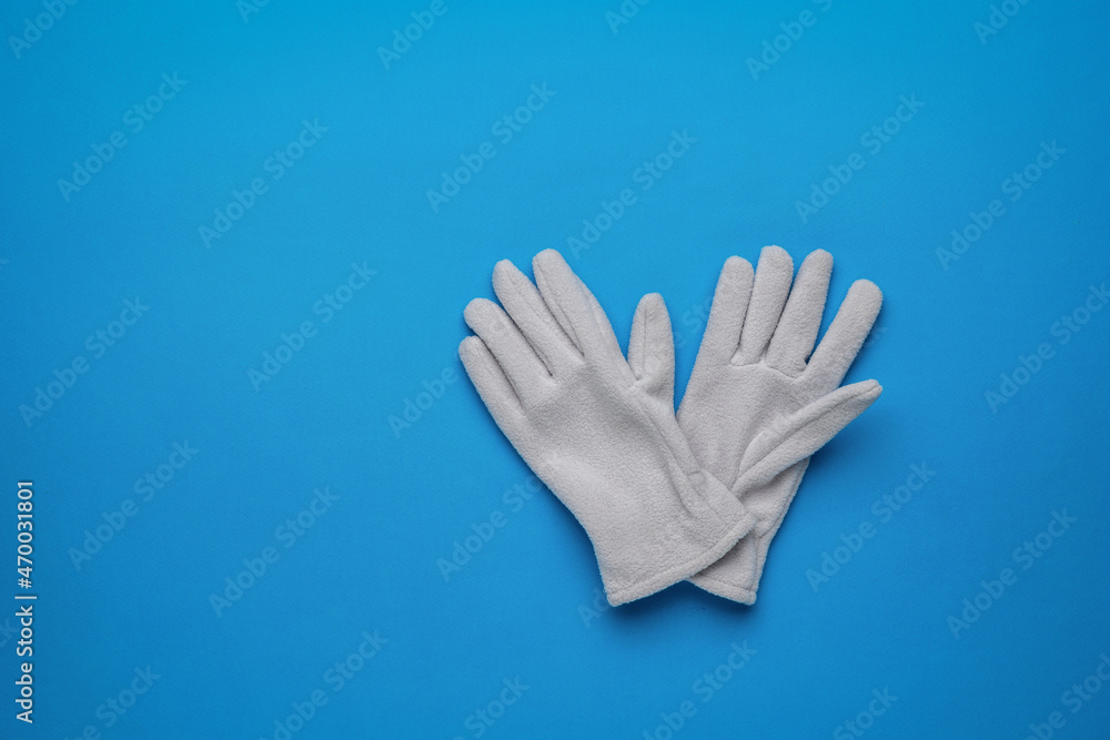 Obraz premium A pair of women's sports-style fleece gloves on a blue background. Flat lay.