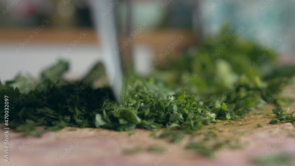 Extreme close up pan woman's hand fast chopping green parsley with an Italian mincing knife sharp knife on a wooden board in her kitchen. Home cooking and healthy food concept Extreme close up pan woman's hand fast chopping green parsley with an Italian mincing knife sharp knife on a wooden board in her kitchen. Home cooking and healthy food concept