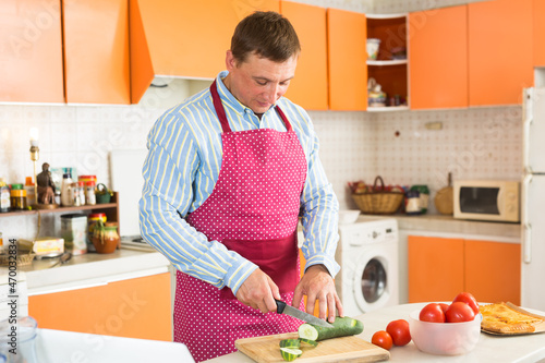 Portrait of adult man cutting vegetables on wooden board in kitchen