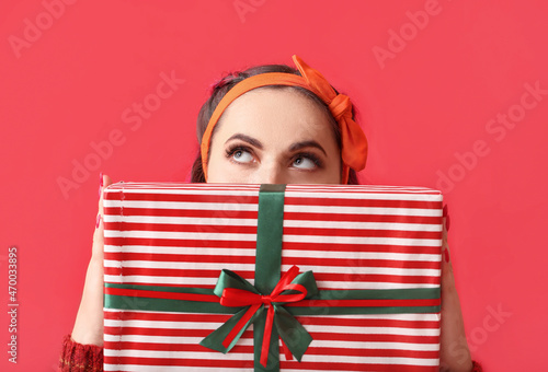 Beautiful woman with Christmas gift on red background