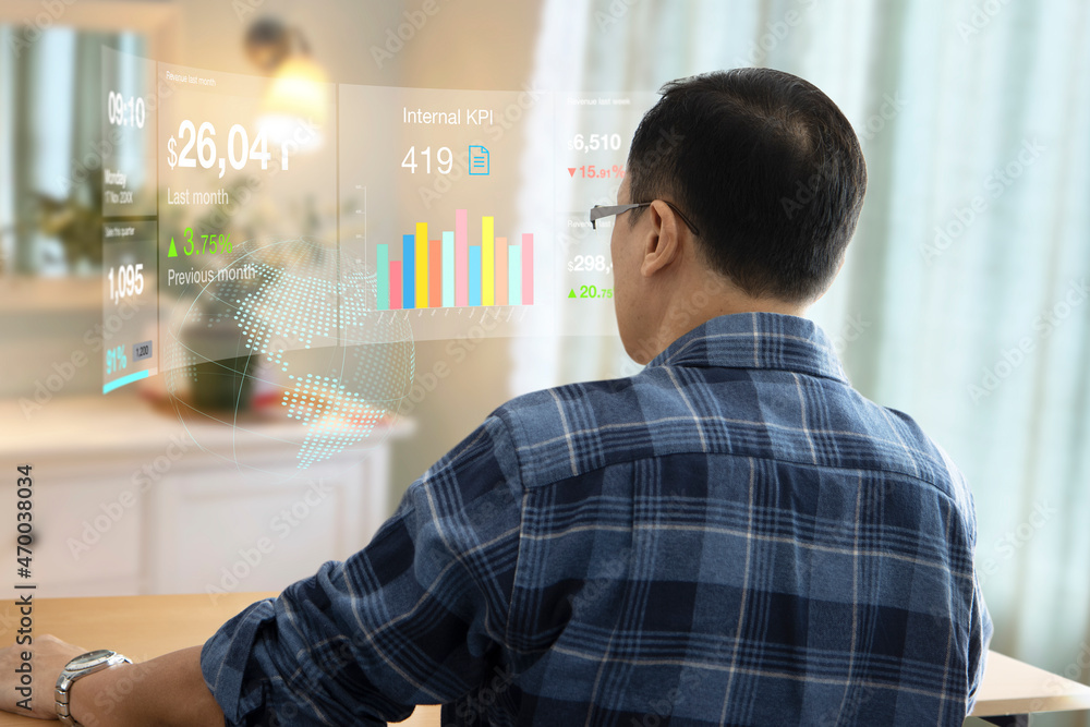 Fototapeta premium Rear view of Asian businessman working from home interacting with virtual reality touch screen on metaverse or computer-generated environment while analysing on business investment and performance.