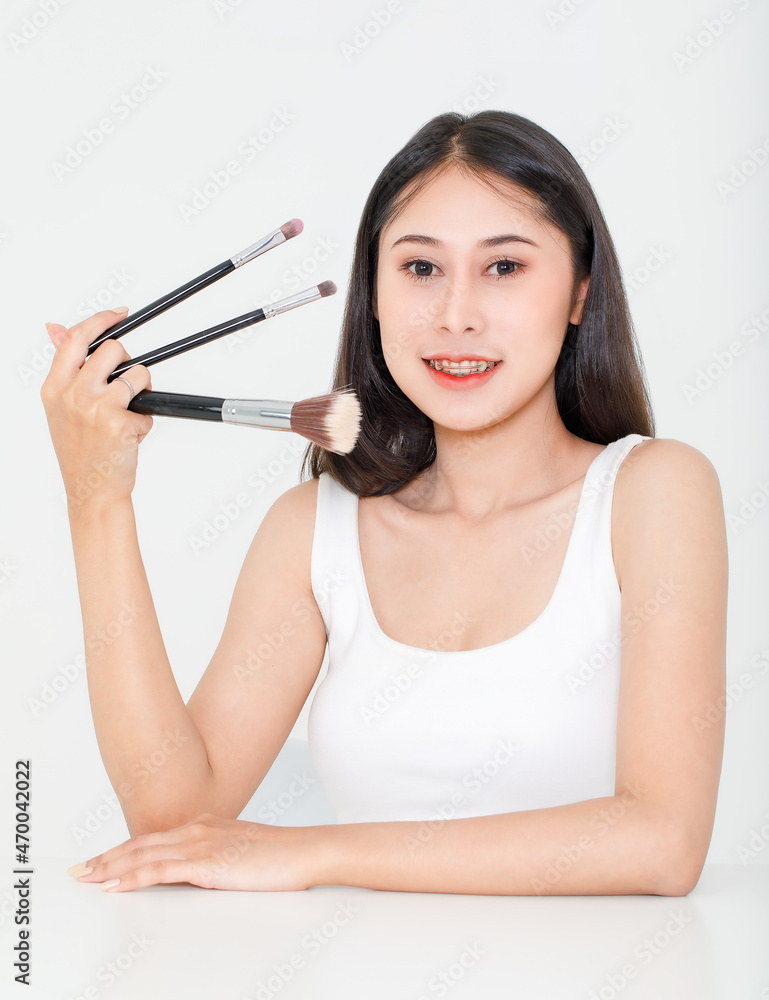 Portrait beauty studio shot of Asian short black hair female model with teeth retainer in tank top vest undershirt hold three size foundation brushes in hand smile look at camera on white background Portrait beauty studio shot of Asian short black hair female model with teeth retainer in tank top vest undershirt hold three size foundation brushes in hand smile look at camera on white background