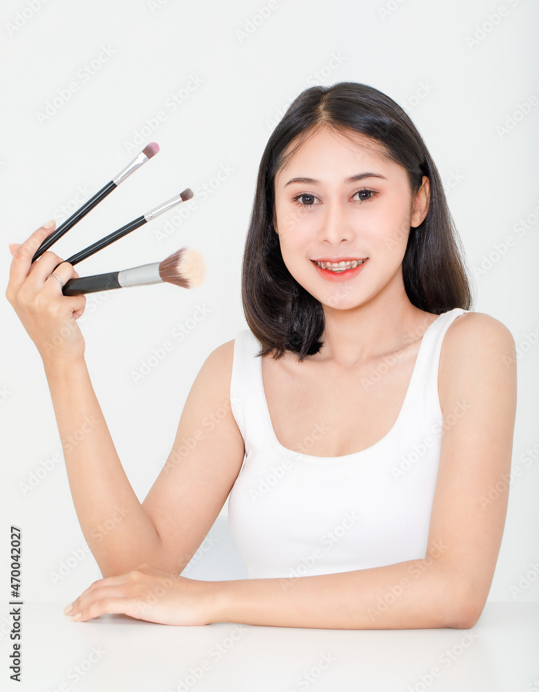 Portrait beauty studio shot of Asian short black hair female model with teeth retainer in tank top vest undershirt hold three size foundation brushes in hand smile look at camera on white background Portrait beauty studio shot of Asian short black hair female model with teeth retainer in tank top vest undershirt hold three size foundation brushes in hand smile look at camera on white background