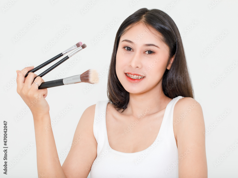 Portrait beauty studio shot of Asian short black hair female model with teeth retainer in tank top vest undershirt hold three size foundation brushes in hand smile look at camera on white background Portrait beauty studio shot of Asian short black hair female model with teeth retainer in tank top vest undershirt hold three size foundation brushes in hand smile look at camera on white background