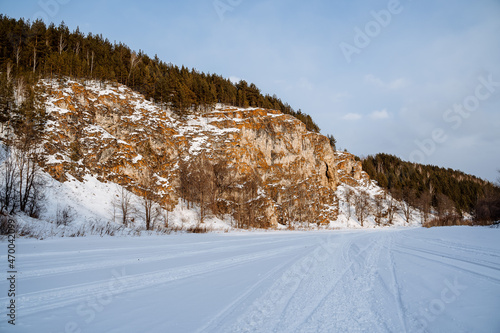 Winter landscape of a rock on the bank of the river. The rocky mountains of orange color are strewn with snow. Cold Russian winter. Ural Mountains