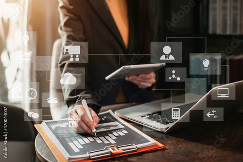 Businesswomen use the tablet and laptop on work papers at the table.