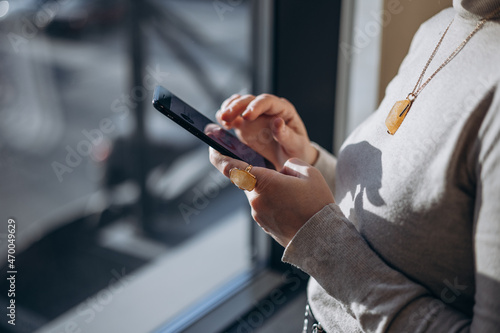 Happy millennial hispanic teen girl checking social media holding smartphone at home. young woman using mobile phone app, shopping online, ordering delivery near window
