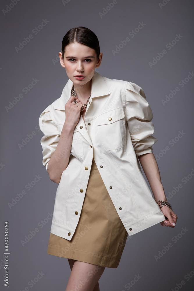 High fashion photo of a beautiful elegant young woman in a pretty white shirt, beige sand skirt,  accessories  posing on gray background. Studio Shot. Slim figure.