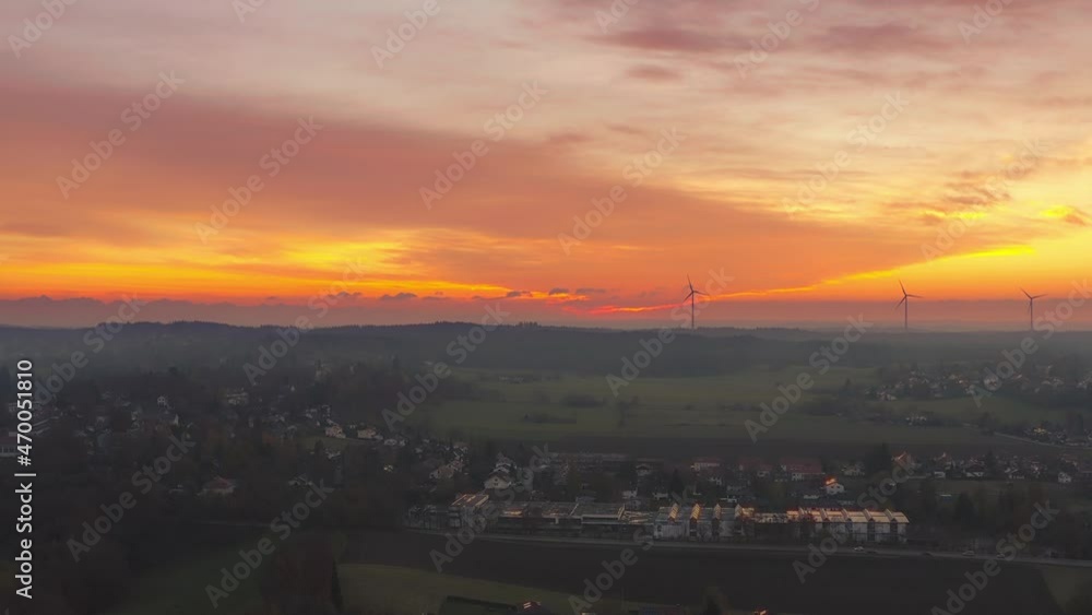 Awesome sunset behind a little rural town with wind turbines in the orange glowing background Awesome sunset behind a little rural town with wind turbines in the orange glowing background