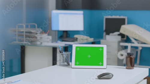 Mock up green screen tablet computer with isolated display standing on table in empty hospital office room. Medial workplace with nobody in it equipped with clinical equipment. Medicine service