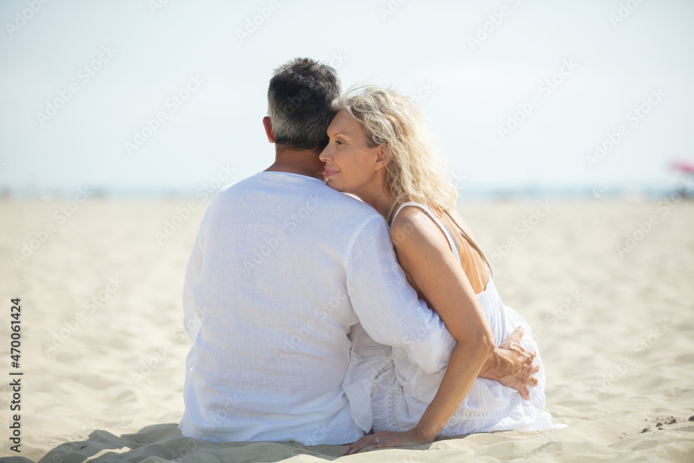 senior couple sat embracing on a deserted beach
