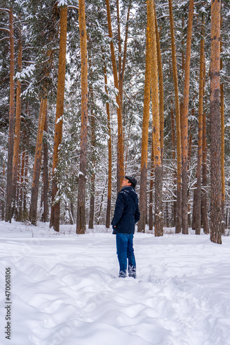 Man walking in winter snow covered forest in cloudy day. Man standing against landscape with pine trees. Human and nature, weekend at countryside, winter vacation concept