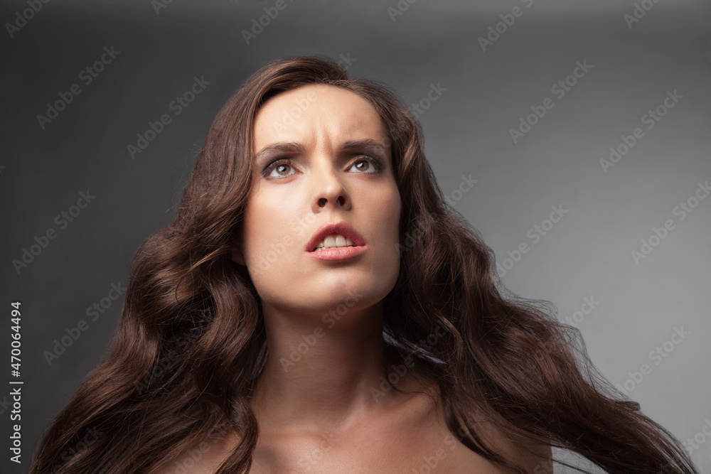 Closeup portrait of a serious lady with long curly hair over gray background Closeup portrait of a serious lady with long curly hair over gray background