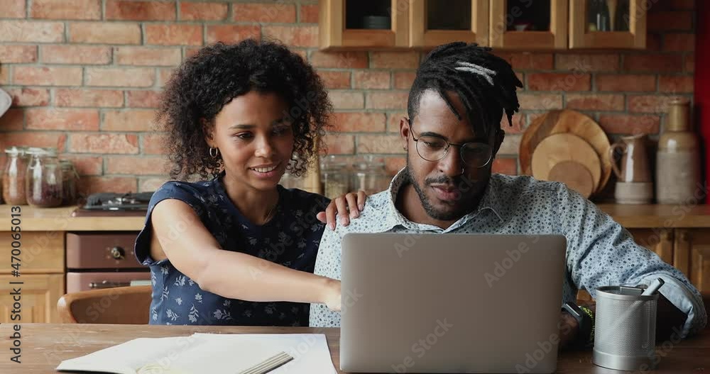 Beautiful African 30s couple sit at table in kitchen make purchase on internet using laptop, discuss order enjoy retail website, pay through e-bank app. Commerce services clients, modern tech concept Beautiful African 30s couple sit at table in kitchen make purchase on internet using laptop, discuss order enjoy retail website, pay through e-bank app. Commerce services clients, modern tech concept