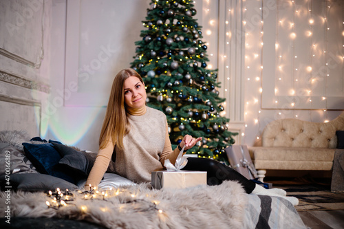 A young woman in a sweater with long beautiful hair sits and laughs in front of Christmas gifts. Happy New Year © Дмитрий Ткачук