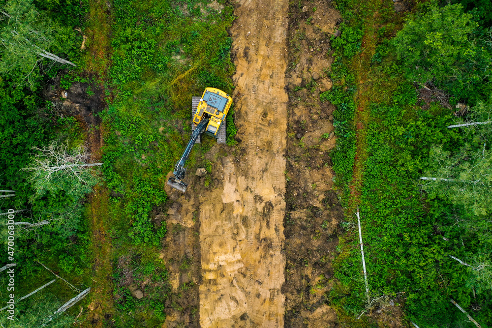 Naklejka premium Top down shot of excavator digging up material through forest for new subdivision.