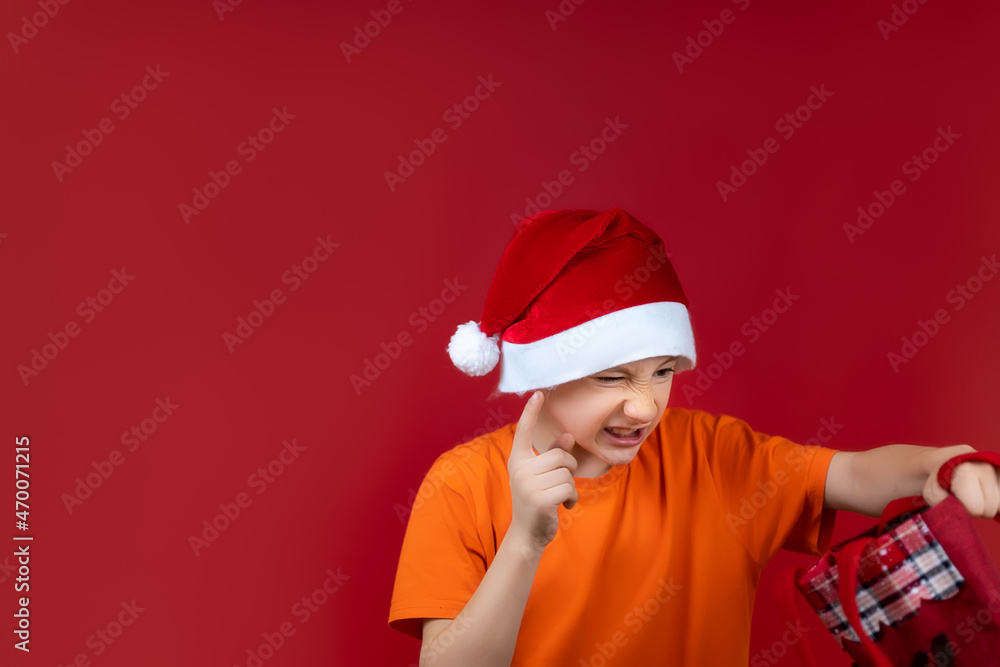 a boy in a Santa Claus Christmas hat holds a gift bag in front of him and shakes his finger a boy in a Santa Claus Christmas hat holds a gift bag in front of him and shakes his finger