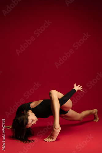 One emotional young flexible contemp dancer, ballerina jumping isolated on dark red background. Art, beauty, inspiration concept.