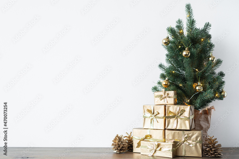 a small Christmas tree with warm bulbs in a pot on a wooden table with gifts wrapped in gold paper. the concept of Christmas