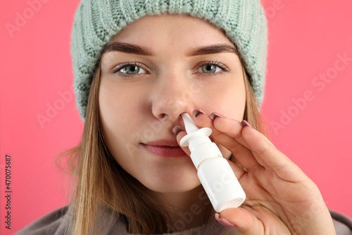 Young woman using nasal spray on pink background, runny nose concept