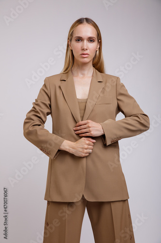 High fashion photo of a beautiful elegant young woman in a pretty beige brown suit, button-down pants, jacket posing over white background. Studio Shot. Slim figure, wide clothes.