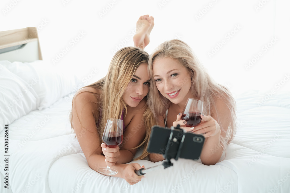 two sexy caucasian women holding selfie stick and a glass of wine two sexy caucasian women holding selfie stick and a glass of wine
