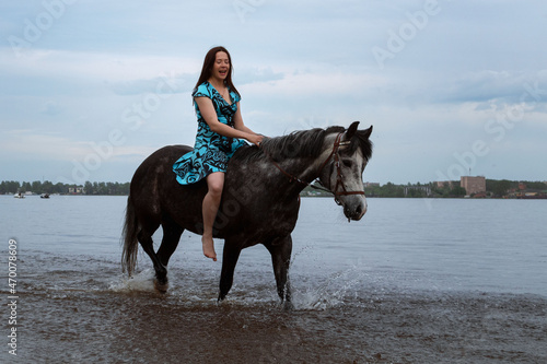 Happy young woman rides a horse on the water