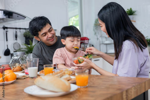 Asian Thai family parents take care young boy kid like to eat vegetable breakfast and drink milk in morning