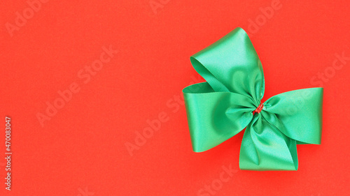 Top view, green tied bow on red background. Space for your text, concept for Christmas decoration..