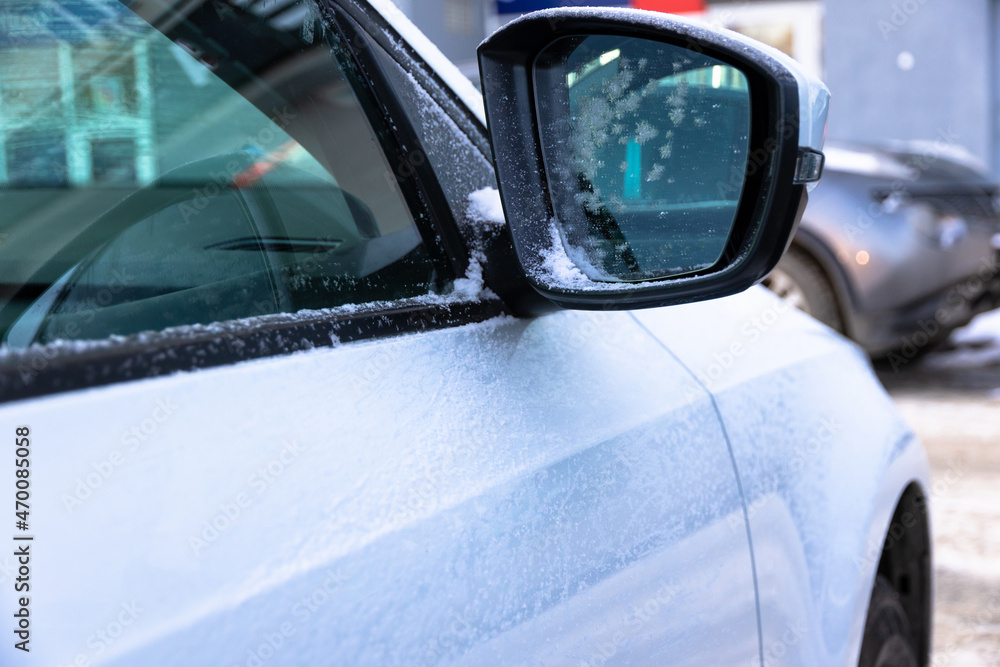 Obraz premium Side mirror of a white new snow-covered car with a reflection covered with frost on a sunny bright frosty day in the Urals. Selective focus. Close-up
