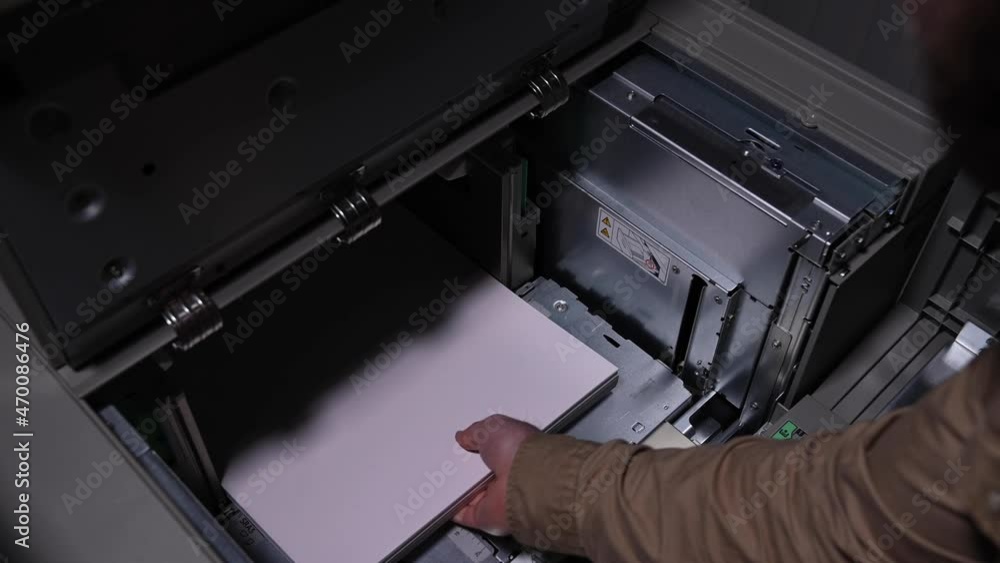 Male businessman worker loading a pack of white paper for printing into an industrial printer Male businessman worker loading a pack of white paper for printing into an industrial printer
