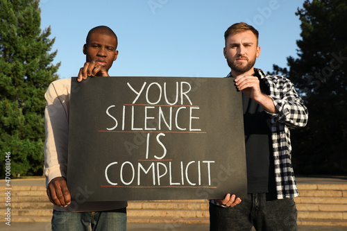 Men holding sign with phrase Your Silence Is Complicit outdoors. Racism concept photo