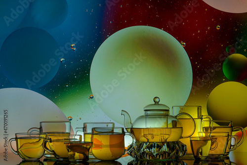 transparent glass teapot and cups with tea and drops on colorful background 