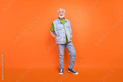 Photo of handsome charming retired man wear vintage jeans waistcoat walking smiling isolated orange color background