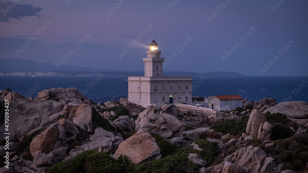 Lighthouse in Capo Testa, Sardinia Italy after sunset. Lighthouse on a rocky shore next to the ocean during dusk. 