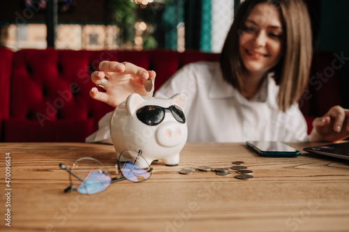 a business woman sits at a table in a cafe and collects coins in a piggy bank