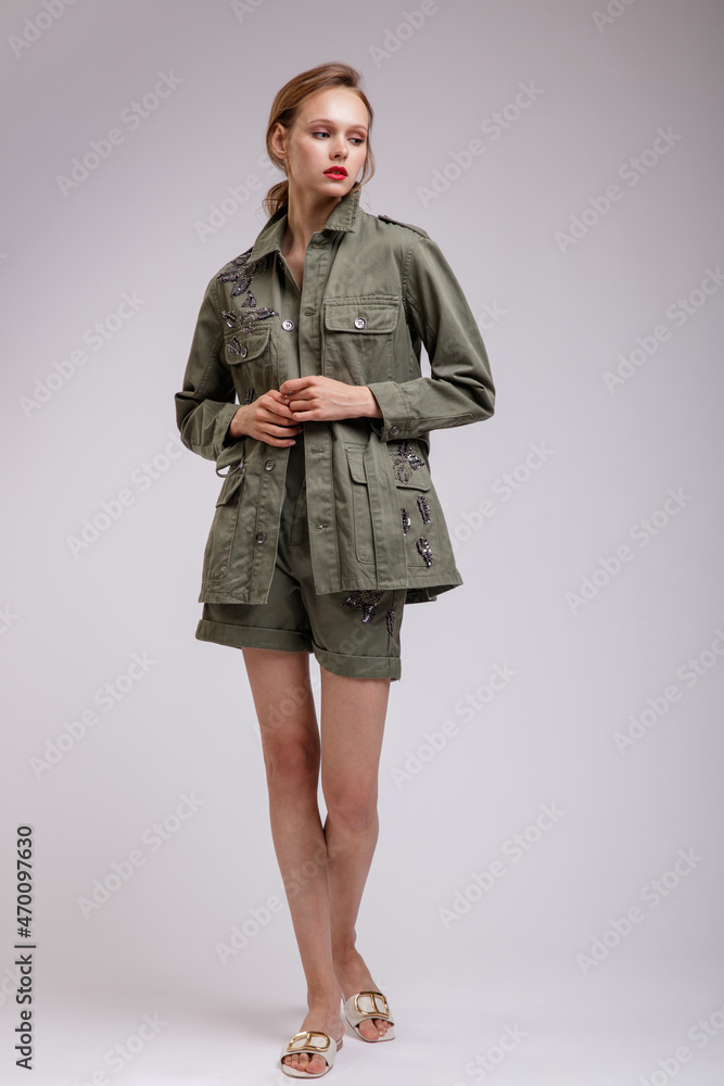 High fashion photo of a beautiful elegant young woman in a pretty green patterned jacket, short shorts posing over white, soft gray background. Slim figure. Studio Shot. High fashion photo of a beautiful elegant young woman in a pretty green patterned jacket, short shorts posing over white, soft gray background. Slim figure. Studio Shot.