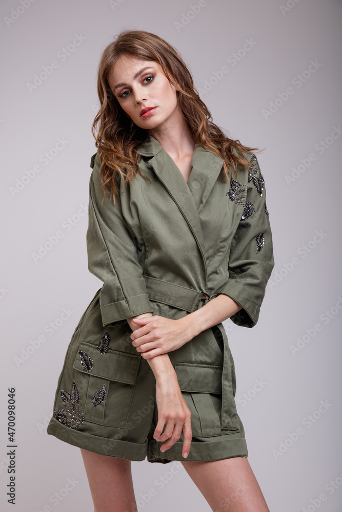 High fashion photo of a beautiful elegant young woman in a pretty green jumpsuit with patterns posing over white, soft gray background. Slim figure. Studio Shot. High fashion photo of a beautiful elegant young woman in a pretty green jumpsuit with patterns posing over white, soft gray background. Slim figure. Studio Shot.