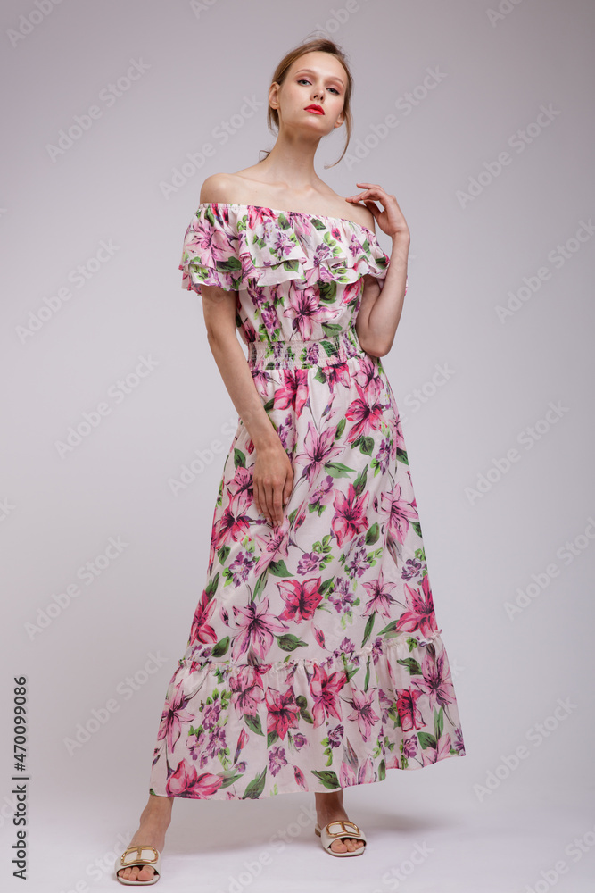 High fashion photo of a beautiful elegant young woman in  pretty long dress with floral patterns in red color posing over white, soft gray background. Slim figure.  Studio Shot. Femininity, tenderness