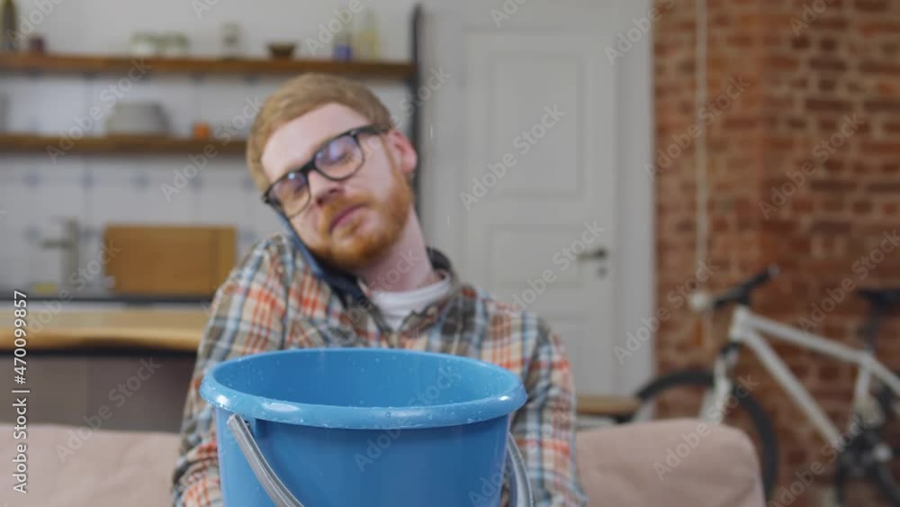 Man calling roof repair service while collecting leaking water from ceiling in living room. Real time Man calling roof repair service while collecting leaking water from ceiling in living room. Real time